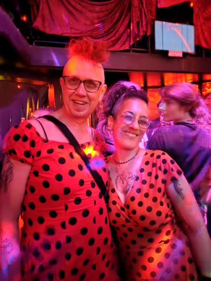 Twee witte queers in rode en oranje polkadotjurk bij rood licht