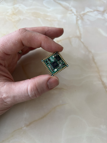 A hand holding a small, stamp-sized circuit board.
