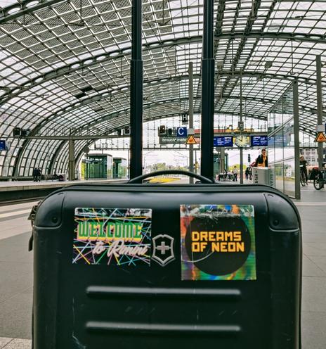 My banged-up suitcase with stickers for Dreams of Neon and Welcome to Rimini, photographed on a platform at Berlin Hbf
