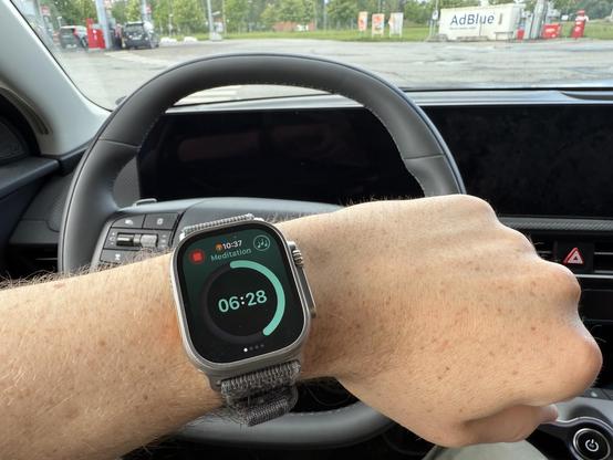 A photo of my wrist with my Apple watch running a Zenitizer meditation. There is a steering wheel of our car in the background as I'm currently taking a fast charging break.