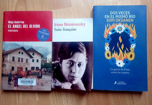 Tres libros colocados uno al lado del otro. El de la izquierda, de tapa roja, muestra la portada de "El Ángel del Olvido" de Maja Haderlap, con la imagen de un pueblo y montañas. El del centro, de tapa blanca, presenta "Suite francesa" de Irène Némirovsky, con un retrato en blanco y negro de la autora. El de la derecha, de tapa azul, muestra "Dos veces en el mismo río" de Sofi Oksanen, con una ilustración de un círculo de flores y llamas, que alude a la guerra de Putin contra las mujeres.