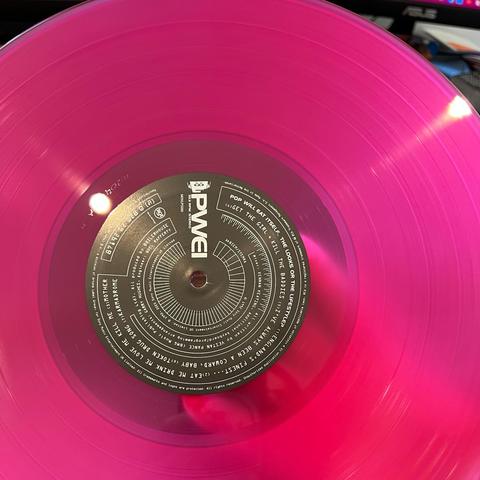 A photo of the vinyl itself of the Music On Vinyl release of Pop Will Eat Itself’s album The Looks Of The Lifestyle. The vinyl is a translucent magenta colour, and you can see my hand through it.