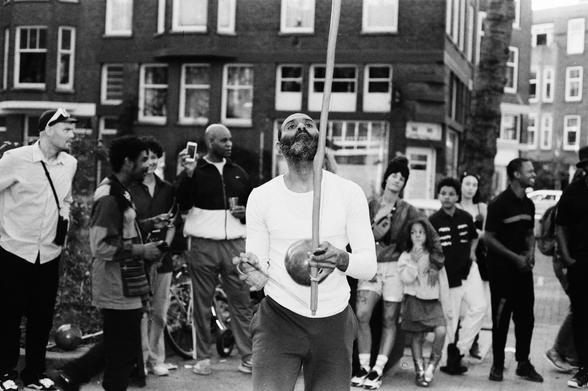 A man in the centre of a circle of people plays the berimbau, announcing a capoeira performance to begin.