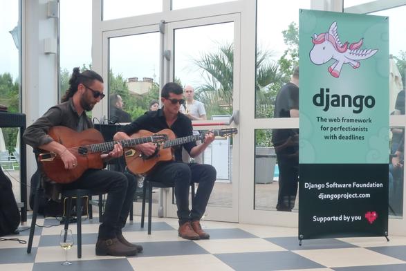 2 musicians with sunglasses, playing acoustic guitars (Django Reinhardt covers) next to a Django roll-up.