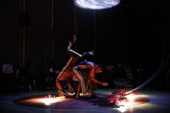 Image: Sweat Variant, Okwui Okpokwasili and Peter Born: let slip, hold sway, 2025. Photography Maria Baranova. Image courtesy the artist and The Whitney Museum of American Art. | two figures performing in a dark space (though there are hints of spectators in the background); two figures wearing what may be red tracksuits, though grotty ones, are interacting, in that one is leaning backwards, hands in the air, onto the back of the other, who is bent forward as though tending to a fire, though the firre is apparently some arrangement of metal and maybe rope, red; strong lights pick out parts o fthe scene, and there appears to be a circular cloudscape projected onto a surface above the figures • “Launching with a major solo exhibition by Sam Gilliam (1933 – 2022), one of the great innovators in post-war American painting…”