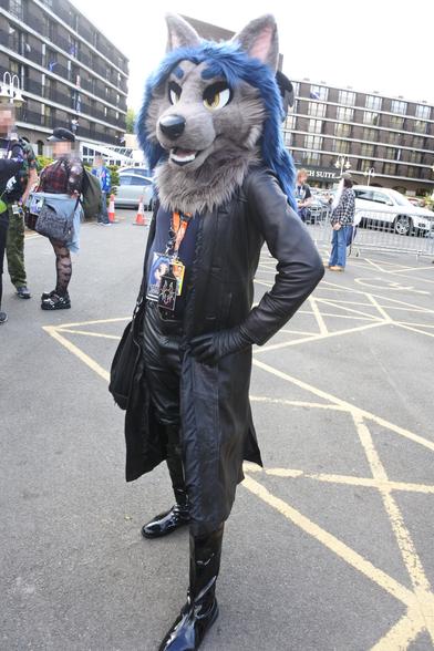 Photo of a wolf fursuiter outside the Hilton at Confuzzled 2025
He is wearing a leather trench coat, leather gloves, leather jeans and long PVC boots.