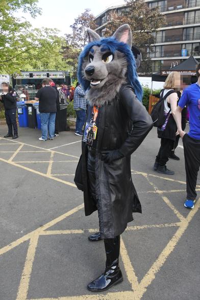 Photo of a wolf fursuiter outside the Hilton at Confuzzled 2025
He is wearing a leather trench coat, leather gloves, leather jeans and long PVC boots.