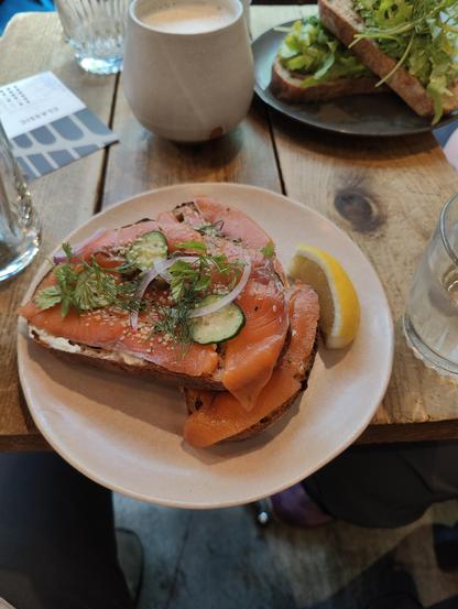 A photo of a meal. Two thick slices of toast are covered with cream cheese, lox, and garnishes.