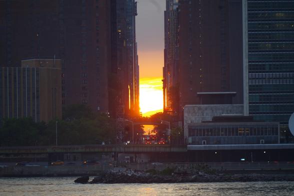 A closer-up shot of the sun setting over 42nd Street. The Tudor City overpass can be roughly seen above the street.