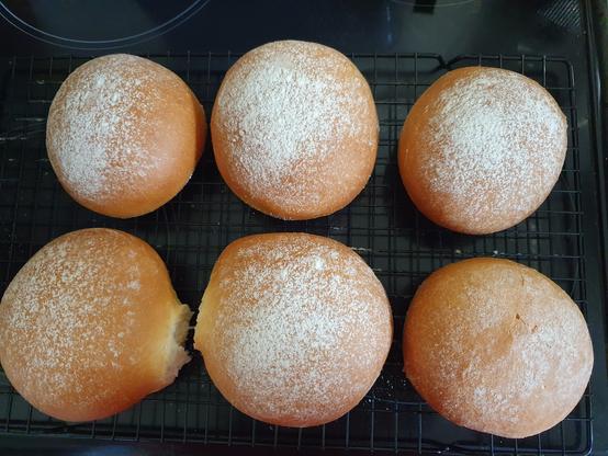 Top down photo of 6 floury bread baps on a baking rack. They're soft and springy to the touch, golden brown with lovely white flour sprinkled in top.