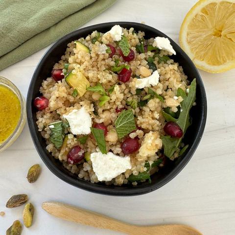 A bowl of arugula quinoa salad with roasted zucchini, goat cheese, pine nuts, and pomegrante.