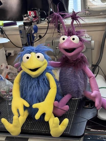 Two full body puppets with fleece heads and fur bodies, one purple with antennae and one yellow with blue fur