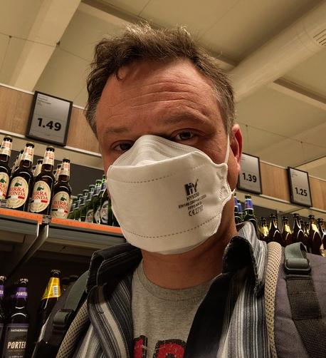 Man wearing FFP3 mask in a supermarket.

Beer bottles are in the background.
