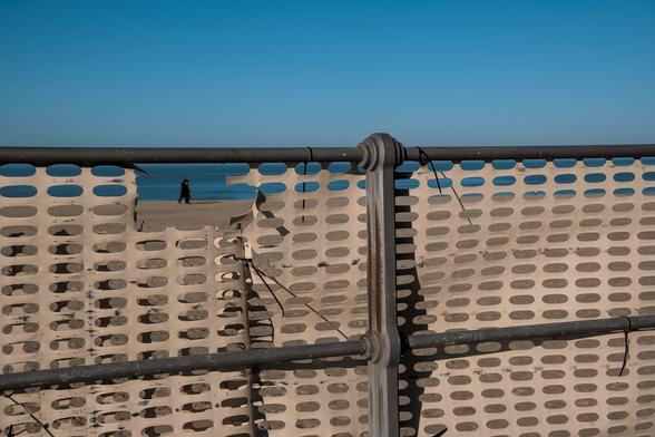 Ostende en hiver. Vue sur le sable, la mer, le ciel bleu et des promeneurs à travers un trou dans la barrière.