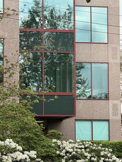 Photo of a section of building featuring two columns of windows.  The column on the left is covered in dark glass with red frames.  The column on the right is made of rose-coloured stone with clear windows, also framed in red.