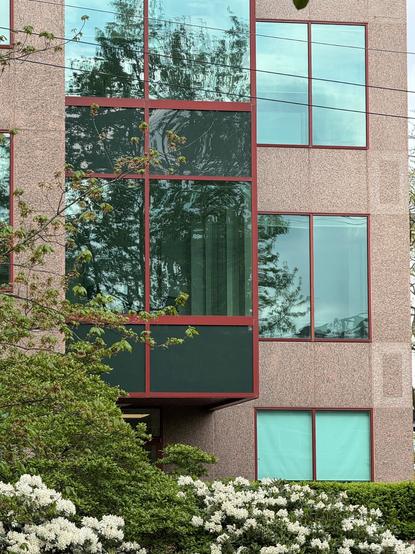 Photo of a section of building featuring two columns of windows.  The column on the left is covered in dark glass with red frames.  The column on the right is made of rose-coloured stone with clear windows, also framed in red.