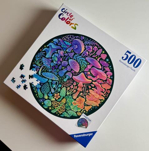 A colorful 500-piece jigsaw puzzle box titled "Circle of Colors" by Ravensburger, featuring intricate designs of mushrooms, plants, and flowers in a circular pattern