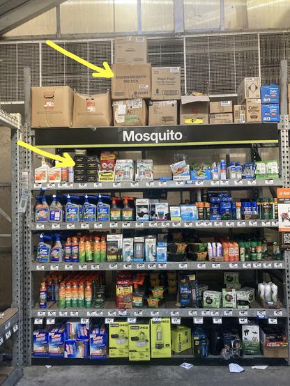 Large metal shelf filled with different products that repel or kill mosquitoes. I've highlighted the location of Spartan Mosquito Pro Techs with yellow arrows. The location on the top shelf is a large box that the devices were shipped in.
