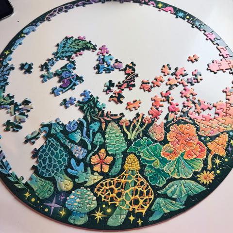 A partially completed round puzzle featuring colorful botanical illustrations, including flowers and leafy plants, with several pieces scattered around