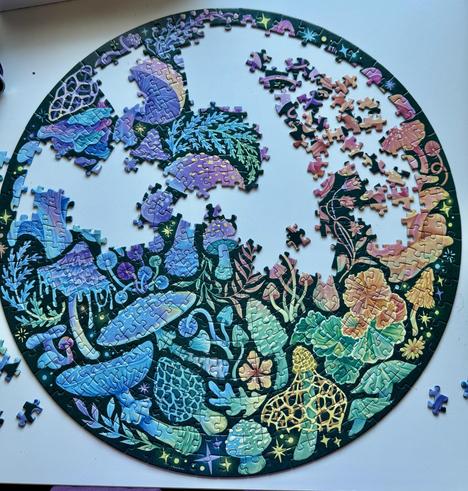 A circular, colorful jigsaw puzzle is partially completed, featuring vibrant illustrations of various plants and mushrooms