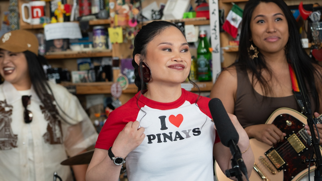 Image of Ruby Ibarra, a Filipina woman, wearing a T-shirt that says "I love Pinays," with a woman on each side of her, one of whom is holding a guitar.