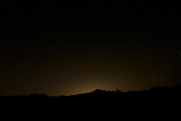 In the darkness there are starts in the sky as well as a golden glow that illuminates the outline of a low ridge.