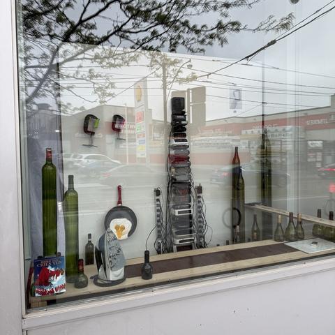 A storefront window display features various bottles and decorative items, with reflections of the street and trees visible on the glass.