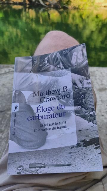 Couverture du livre "Éloge du carburateur.  Essai sur le sens et la valeur du travail" de Matthew B. Crawford. On y voit, en noir et blanc, un gros plan sur quelqu'un travaillant sur le moteur d'une moto, avec une tache d'huile et des outils au sol.