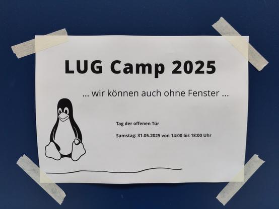 Flyer auf einer Tür mit dem Text: LUG Camp 2025 - Wir können auch ohne Fenster. Tag der offenen Tür, Samstag 31.05.2025 von 14 bis 18 Uhr.