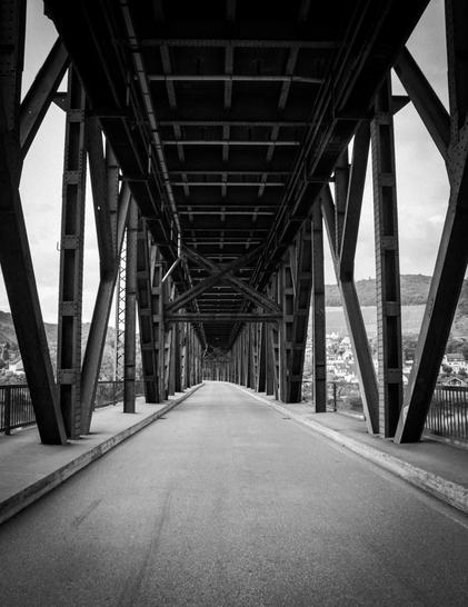 a black and white picture of a bridge which has train tracks above.