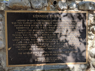KENNEDY TUNNEL

OPENED IN 1903, THE TIMBER-LINED KENNEDY TUNNEL WAS THE FASTEST ROUTE BETWEEN OAKLAND AND LAFAYETTE SAVING FOUR HOURS OF DRIVING AROUND THE SAN PABLO RESERVOIR. IN 1914, IT WAS WIRED FOR LIGHTS AND RENAMED THE BROADWAY TUNNEL. IN 1937, AFTER THE COMPLETION OF THE CALDECOTT TUNNEL THE KENNEDY TUNNEL WAS CLOSED TO MOTOR CARS, ALLOWING ONLY FOOT, HORSE AND TWO-WHEELED TRAFFIC. IN 1947. THE TIMBER LINED TUNNEL WAS PERMANENTLY CLOSED DUE TO REPEATED CAVE-INS AND RISING MAINTENANCE COSTS. IT FINALLY SUCCUMBED TO NATURE IN THE LATE 1960'S AND THE MEDIAN LOCATED AT THE INTERSECTION OF OLD TUNNEL RD. AND SKYLINE DR. IS THE ONLY REMNANT EXISTING TODAY

THE MEDIAN STILL HOLDS THE ORIGINAL DEDICATION PLAQUE AND FLAGPOLE.

DEDICATED JULY 10, 2010 (6015) 
JOAQUIN MURRIETA CHAPTER 
E. CLAMPUS VITUS