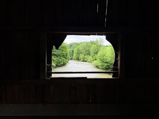 der fluss und die grünen bäume durch ein fenster in der holzbrücke gesehen