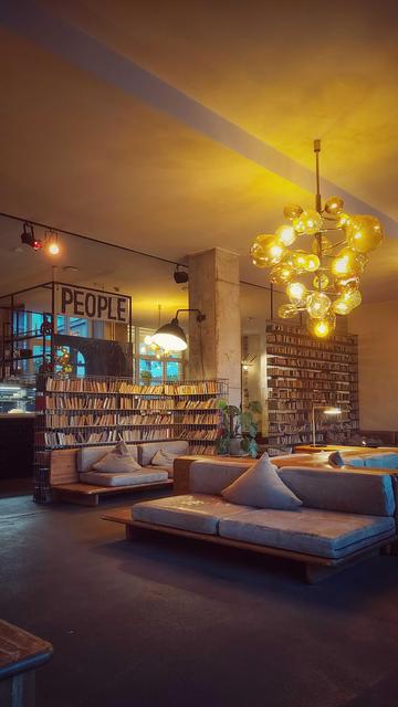 A hotel lobby. Warm lights, low couches, books in shelves. A banner reading PEOPLE.