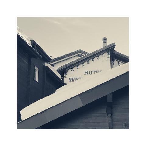a look over some stacked gabled roofs. on some of the roofs there's still some white snow. there's also a chimney, a white window and parts of some lettering visible