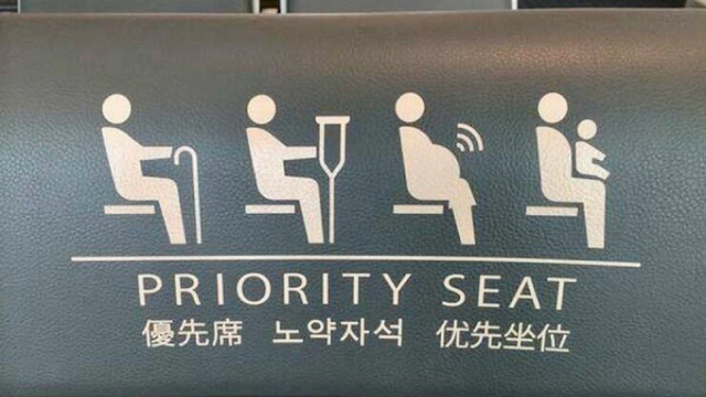Priority seat signage with pictograms showing reserved seating for the elderly, injured, pregnant (with wi-fi waves seeming to emanate from her belly), and those with young children. Text is displayed in multiple languages.