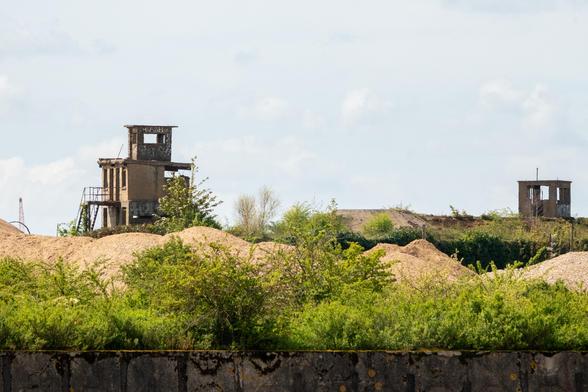 Two buildings rise from piled sand or other construction material. They're blocky, damaged, and covered in graffiti.