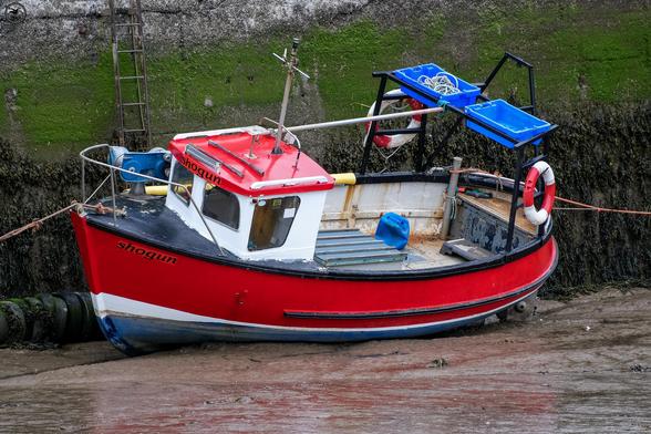 red small fishing boat at rest in muddy low water harbour