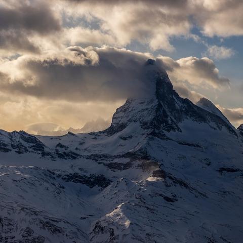 Snow-capped  Matterhorn under a cloudy sky, with sunlight breaking through the clouds, creating dramatic lighting and shadows on the landscape.