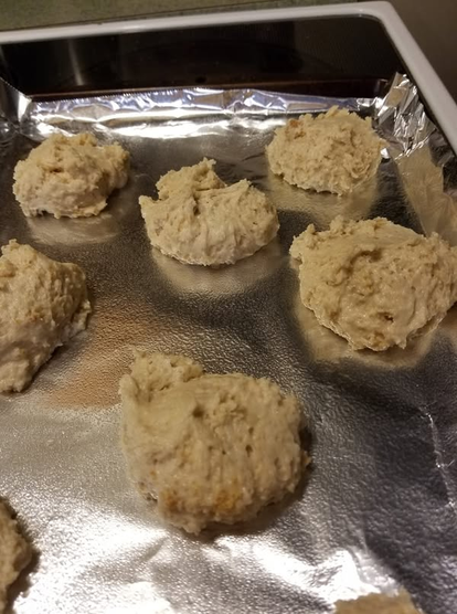a baking sheet covered with aluminum foil hold scoops of unbaked biscuit dough. They were graham cracker shortcakes for an ice cream dessert.