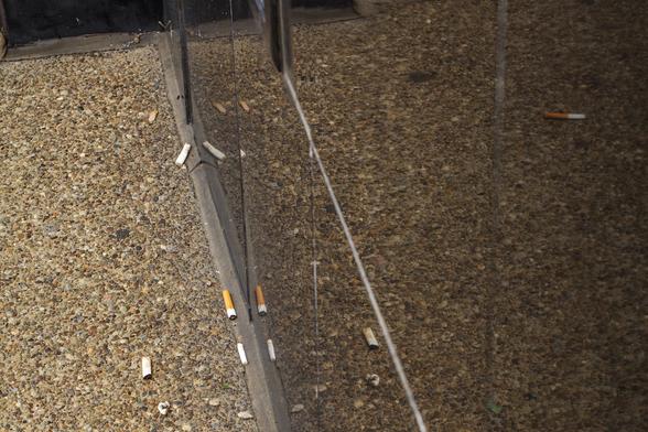 Discarded cigarette butts on a concrete sidewalk is reflected in a building's door and window glass where it meets the sidewalk.