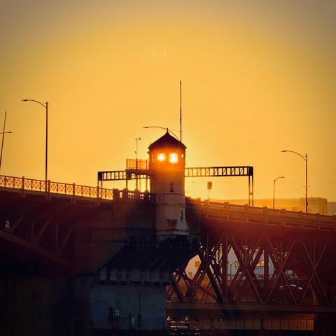 The rising sun is seen shining brightly through two windows in one of the Burnside Bridge control towers on a bright orange, clear morning.
