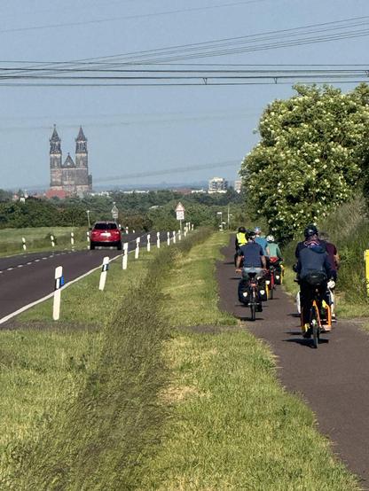 Eine Gruppe Fahrradfahrer fährt auf einem straßenbegleitenden Radweg. Im Hintergrund der Magdeburger Dom