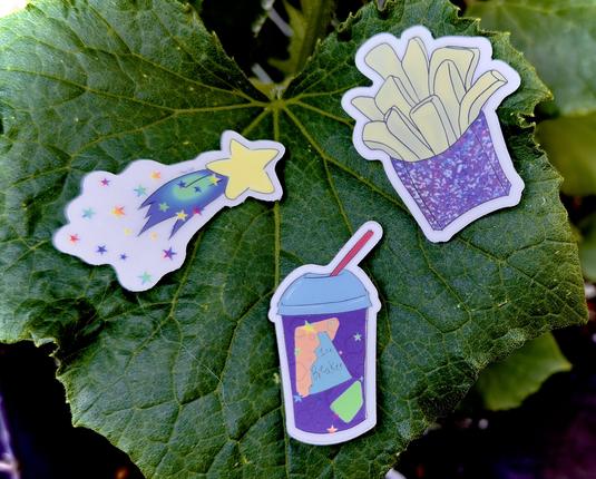 using a cucumber leaf as a display, three stickers are laid out. a see through shooting star, a drink sticker called ice breaker, and the original glitter fry sticker that I originally created