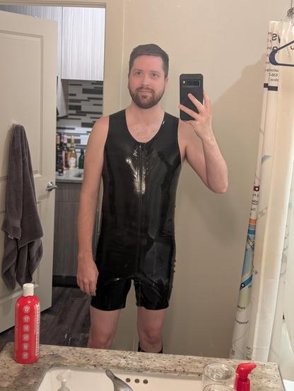 White person with a beard wearing a solid black rubber surf suit in the bathroom
