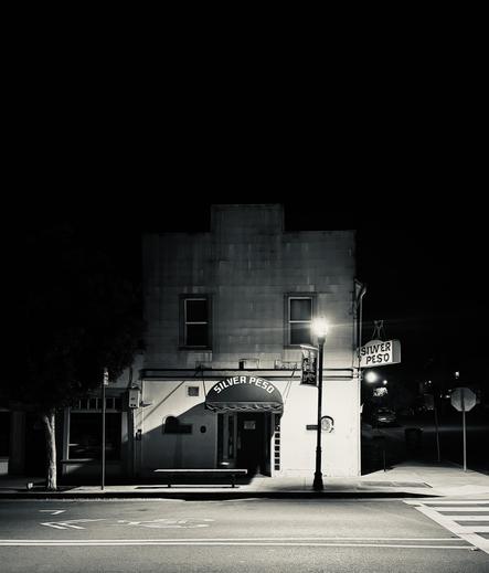 a partially lit closed bar. there is a single street light outside, the street is quiet, car and people free.