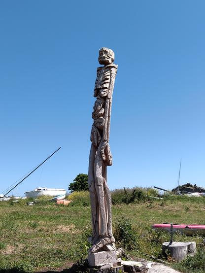 Statue en bois au bord de la mer représentant u' personnage quasi squelettique.