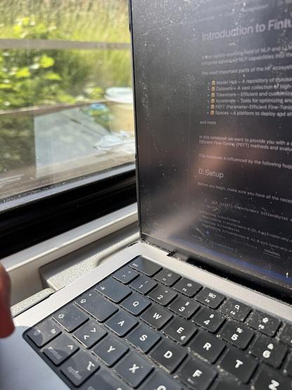 A laptop keyboard and part of the screen displaying a document titled "Introduction to Finetuning" in a workspace. In the background, there are blurred items and greenery visible through a window of the train.