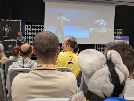 Plush donkey looking at a presentation showing a frame from Star Wars, with the presenter next to it.