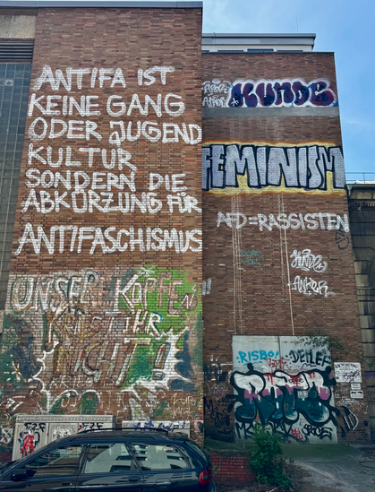 Politische Statements auf einer roten Backsteinfassade:
Antifa ist keine Gang oder Jugendkultur, sondern die Abkürzung für Antifaschismus
darunter (schwer zu lesen da schon etwas verblasst) Unsere Köpfe kriegt ihr nicht!

Daneben als Graffiti
Feminism
und nochmal in weiß: AFD = Rassisten