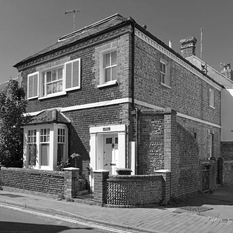 Monochrome photo of a dwelling built early C19 according to the Grade 2 listing. Façade of coursed cobbles with red-brick dressings, quoins and dentils. Entrance with Doric pilasters. Rottingdean, City of Brighton & Hove, UK.